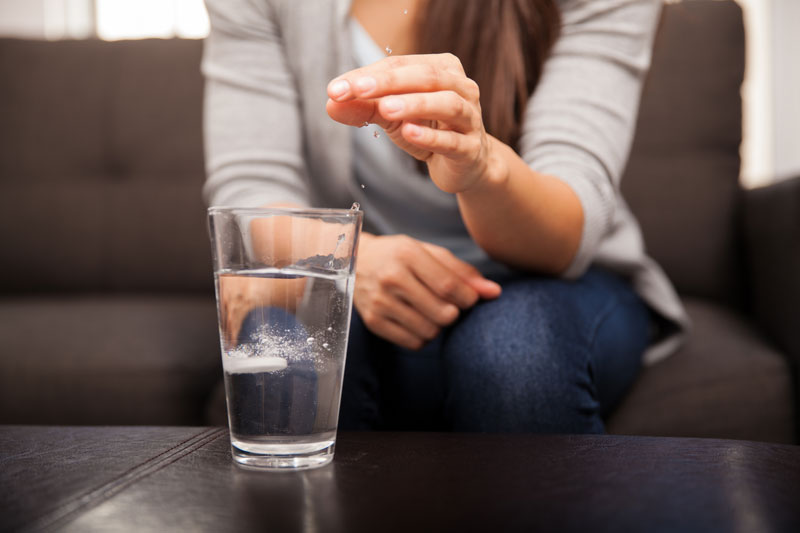 A woman dropping an antacid into a glass of water