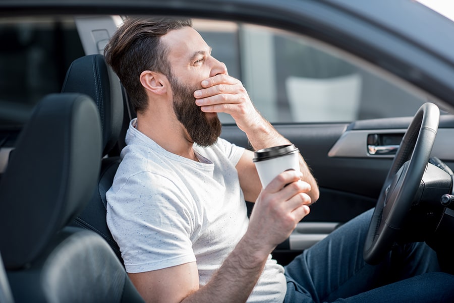 Driving man yawns holding coffee in Jacksonville
