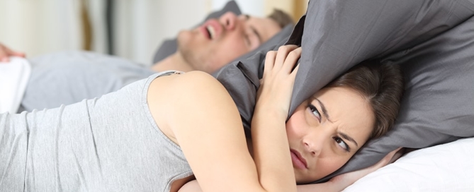 woman covering her ears while her husband snores