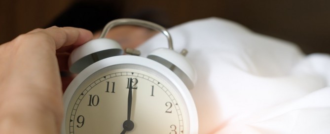 Person in bed holding an alarm clock.